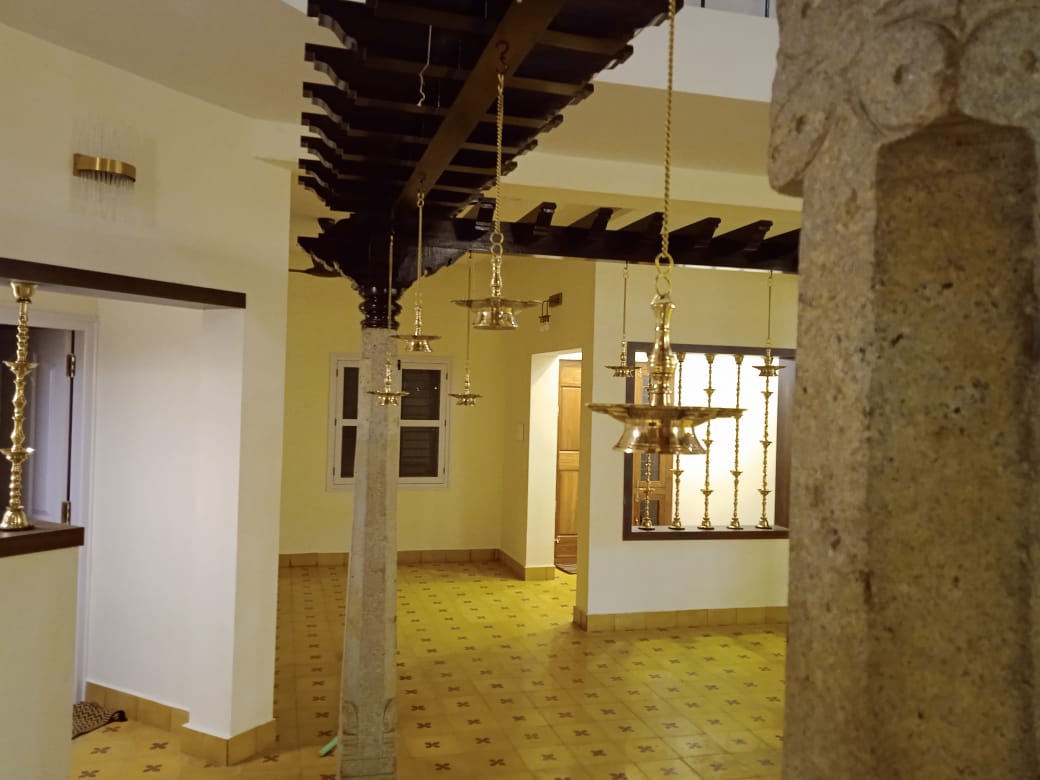Hanging brass Kuthu Vilakku lamps under a wooden pergola beam in Chettinadu style Mysore home